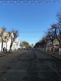 Road by buildings against clear blue sky