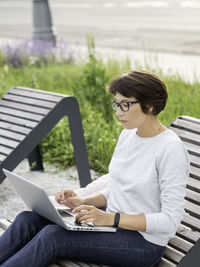 Woman sits with laptop on urban park bench. freelancer at work. student learns remotely. lifestyle.
