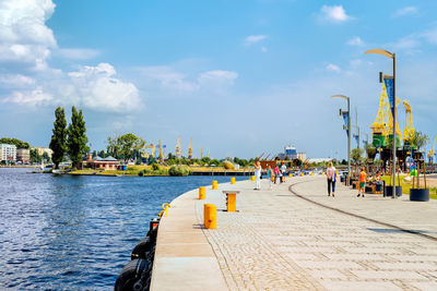 People by boats in river against sky