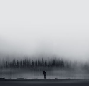 Distant view of silhouette male hiker standing against trees during foggy weather