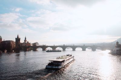 Boat moving towards charles bridge in vltava river against cloudy sky