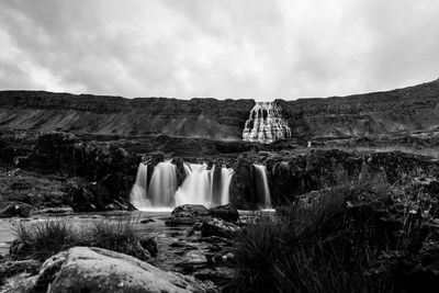 Scenic view of waterfall against cloudy sky