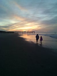 Silhouette people on beach against sky during sunset