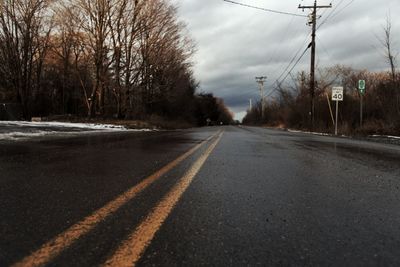 Road by bare trees against sky during winter