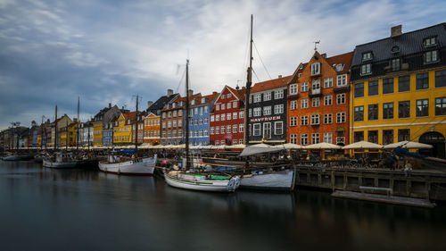 Boats moored in canal by buildings against sky