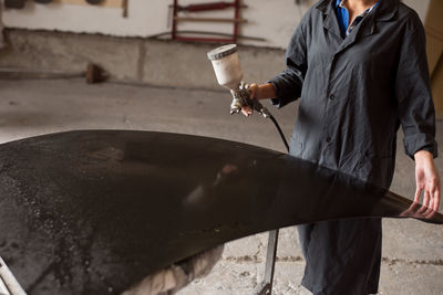 Midsection of female worker painting car at workshop