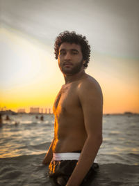 Young man standing on beach against sky during sunset