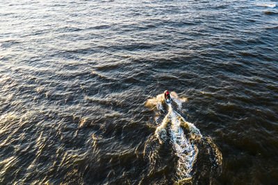 Aerial view of man rides on fast water scooter jumping on waves and making golden splashes on sunset