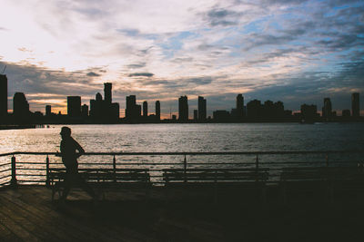 Rear view of silhouette man standing by railing against buildings in city