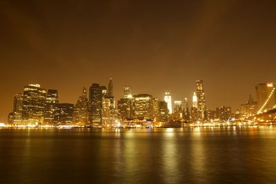 Illuminated buildings by river against sky at night