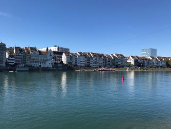 Buildings by sea against clear blue sky