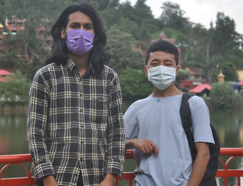 Two male friends with wearing face mask standing outside with looking at camera