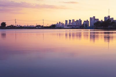 Scenic view of lake by buildings against sky during sunset