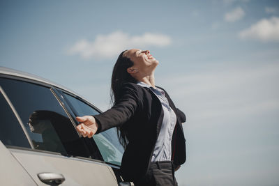 Carefree businesswoman smiling while standing with arms outstretched against sky