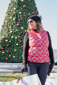 Young woman standing by christmas tree during winter