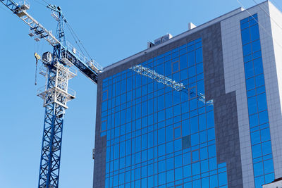 Low angle view of crane by building against clear blue sky