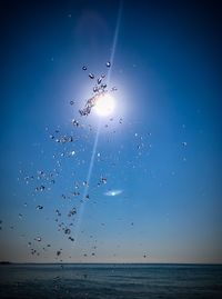 Drops flying over sea against blue sky