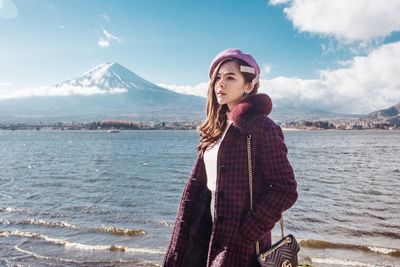 Young woman standing by sea against mountains during winter