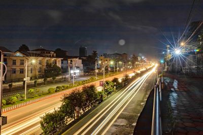 Light trails on street amidst illuminated buildings in city at night