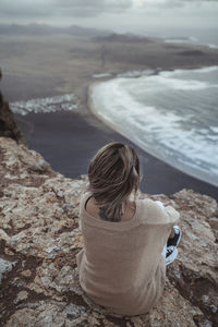 Rear view of woman sitting on rock at beach