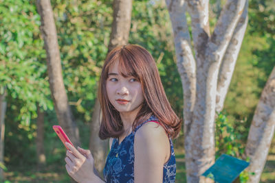 Portrait of young woman standing against tree