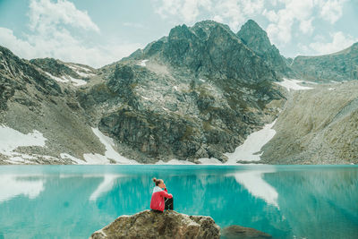 Man sitting on mountain by lake against sky