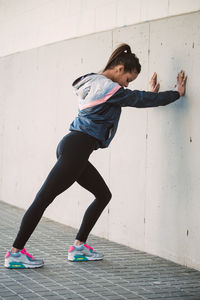 Full length of woman exercising while leaning on wall