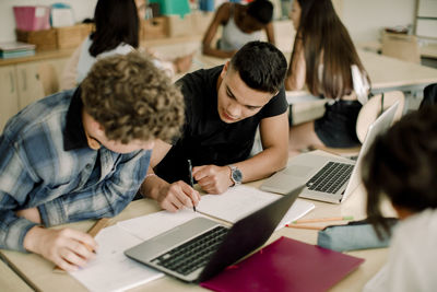 Male students studying at table while female friends sitting in background