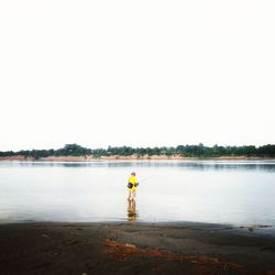 Rear view of man standing at beach against clear sky