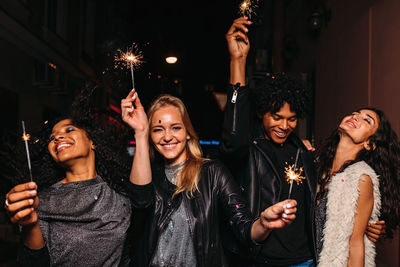 Smiling friends holding lit sparklers in party