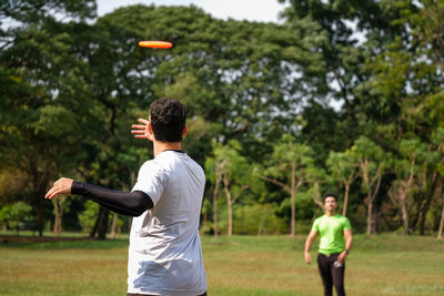 Rear view of man playing with arms raised against trees