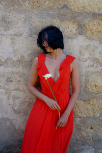 Woman holding flower standing by wall