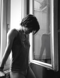 Young woman standing against window at home