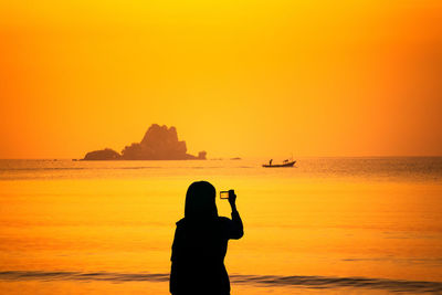 Silhouette man on sea against sky during sunset