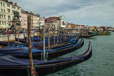 Boats moored in canal amidst buildings against sky