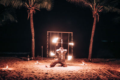 Man sitting on illuminated fire against trees at night