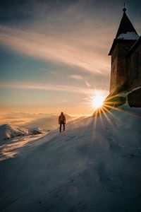 Man on snow amidst buildings against sky during sunset