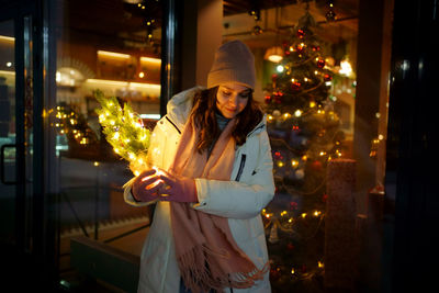 Caucasian white girl near a shop window, with a christmas tree in her hands, garlands are branching