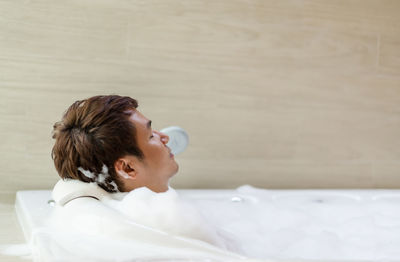 Side view of young woman blowing bubbles while lying on bed at home