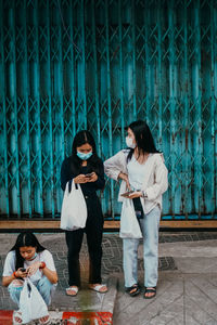 Full length of young woman using phone while standing outdoors