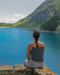 Rear view of woman sitting on rock against sky