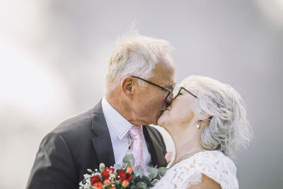 Affectionate senior couple kissing on mouth against wall