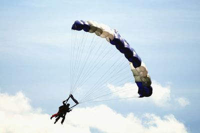 Low angle view of people paragliding against blue sky