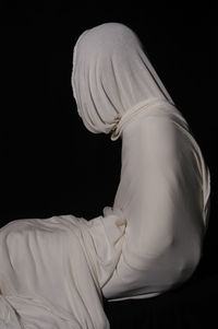 Person wrapped in white fabric against black background