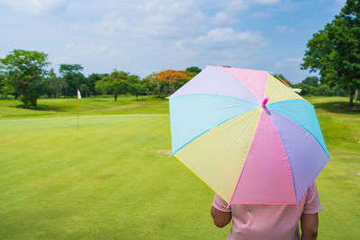 Rear view of woman with umbrella on field against sky