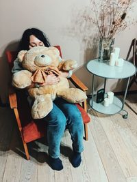 Woman with teddy bear sitting on chair at home