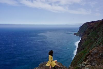 People sitting on rock by sea against sky