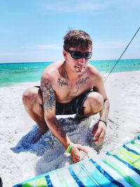 Shirtless man smoking cigarette while playing with sand at beach