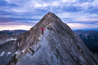 Rear view of female hiker standing on mountain ridge with arms outstretched