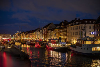 Sailboats moored on illuminated canal by buildings in city at night
